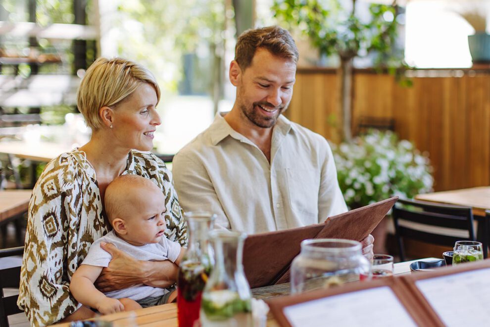 Family with baby reading menu in a restaurant, choosing food and drinks.
